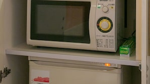 Un microondas sobre una estantería, encima de un mueble, con una vitrina de cristal que contiene varios objetos.