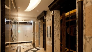Un moderno vestíbulo de hotel con suelos de mármol, puertas de ascensor de vidrio y un diseño de pared curva.