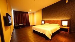 A hotel room with a large bed, wooden flooring, a flat-screen TV, and a wall-mounted lamp. - Merlin Hotel (Port Dickson)