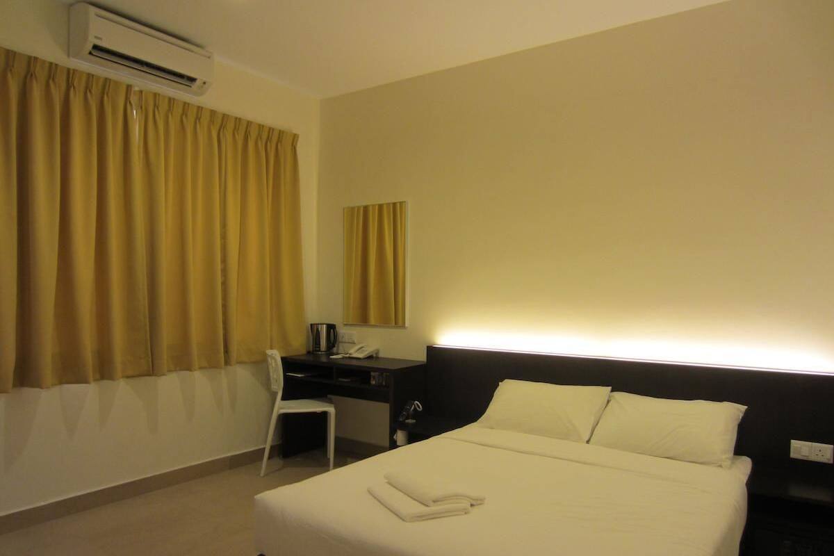 A hotel room with a bed, a desk, a chair, an air conditioning unit, and a window with curtains.