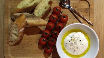 Una tabla de madera con pan en rodajas, tomates cherry y un bol de aceite de oliva y salsa blanca.