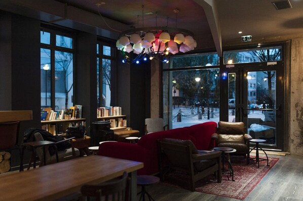 Un acogedor interior de cafetería con un sofá rojo, mesas de madera y una estantería llena de libros.
