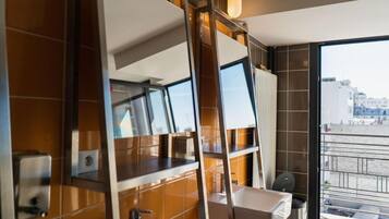 A modern bathroom with a large mirror, a sink, and a window offering a view of the city.