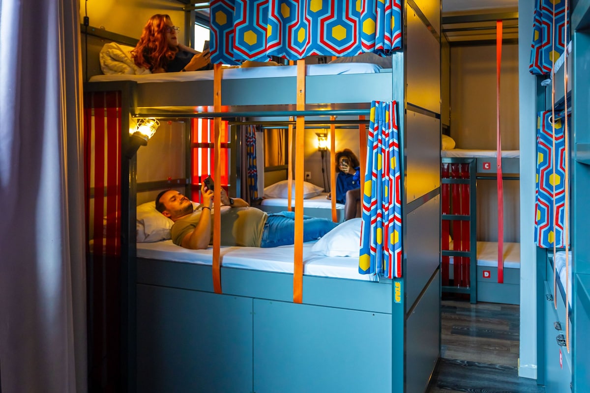 A bunk bed room with a patterned curtain, a wooden floor, and a ceiling light.