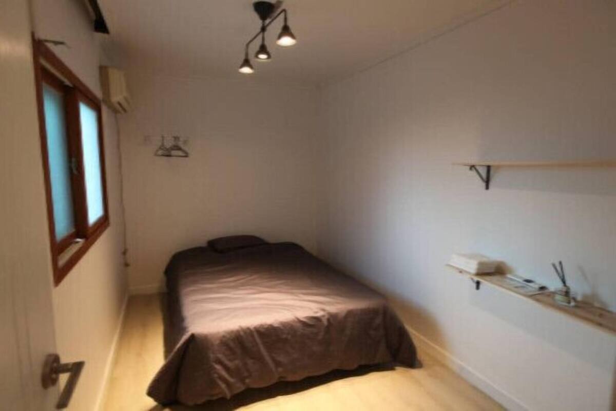 A small, narrow room with a bed, a window, and a shelf with items.