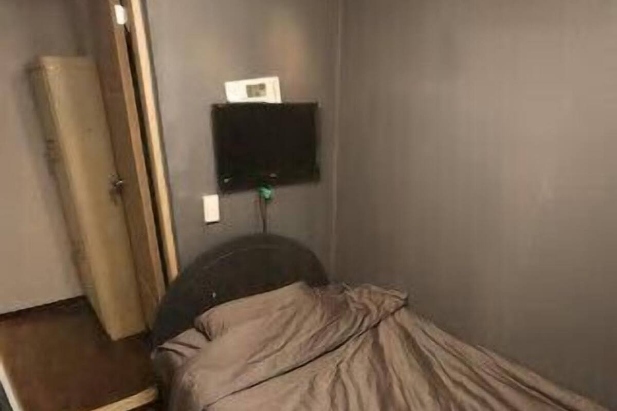 A small, compact room with a single bed, a wooden door, and a wall-mounted TV.