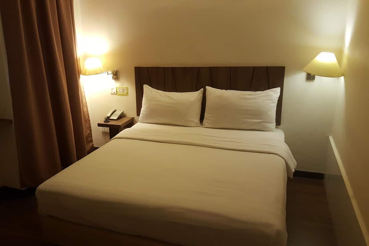 Una habitación de hotel con cama, cortinas, mesita de noche y dos lámparas de pared.
