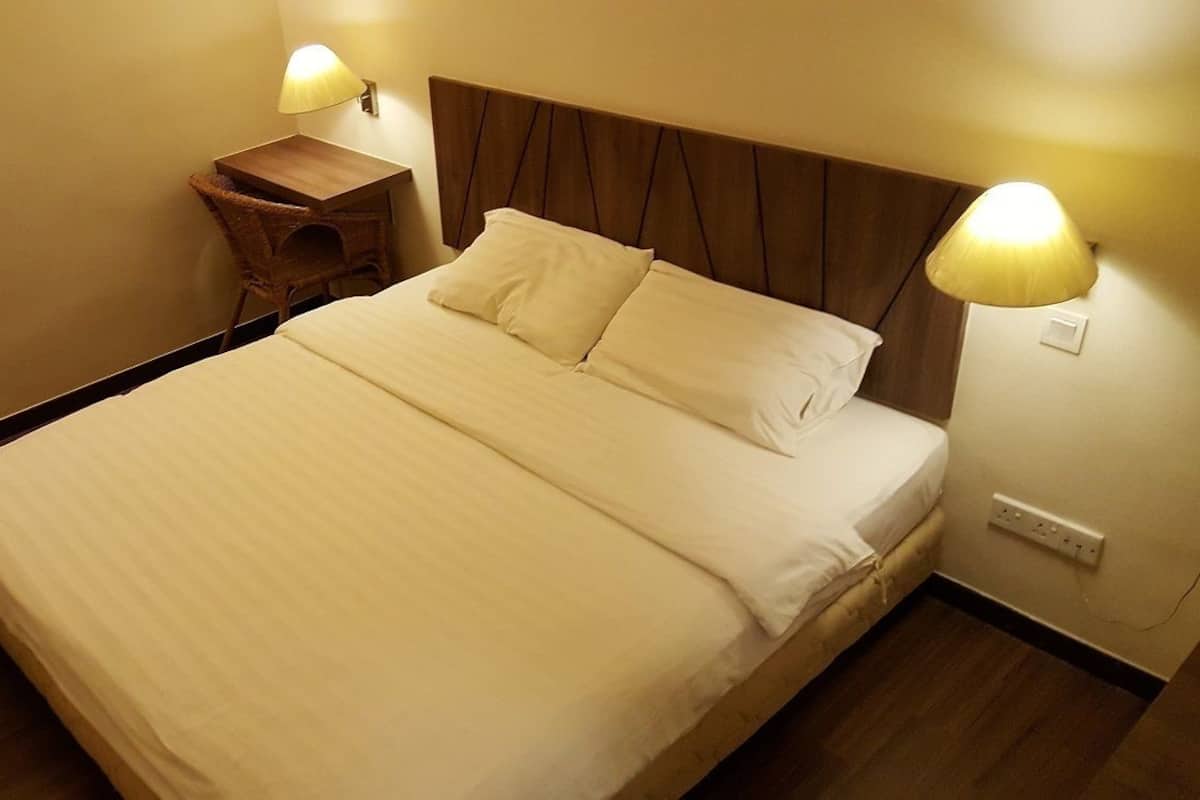 Una cama bien hecha con sábanas blancas, un cabecero de madera y dos lámparas de noche.