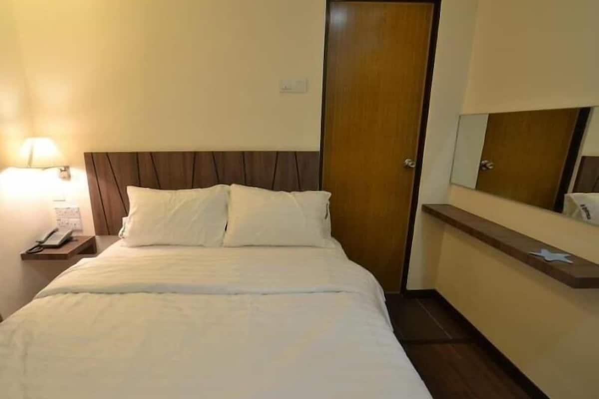 Una habitación de hotel con una cama, una mesita de noche con teléfono, un cabecero de madera, una puerta y un espejo sobre la cama.