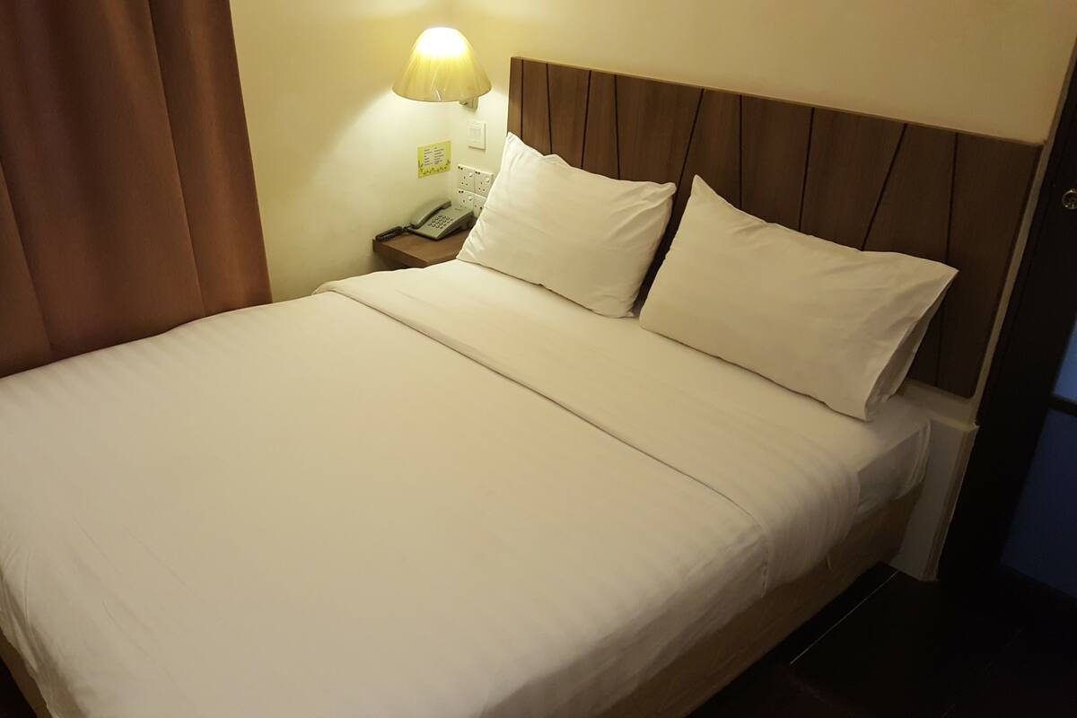 Una cama bien hecha con sábanas blancas, un cabecero de madera y una lámpara de noche.