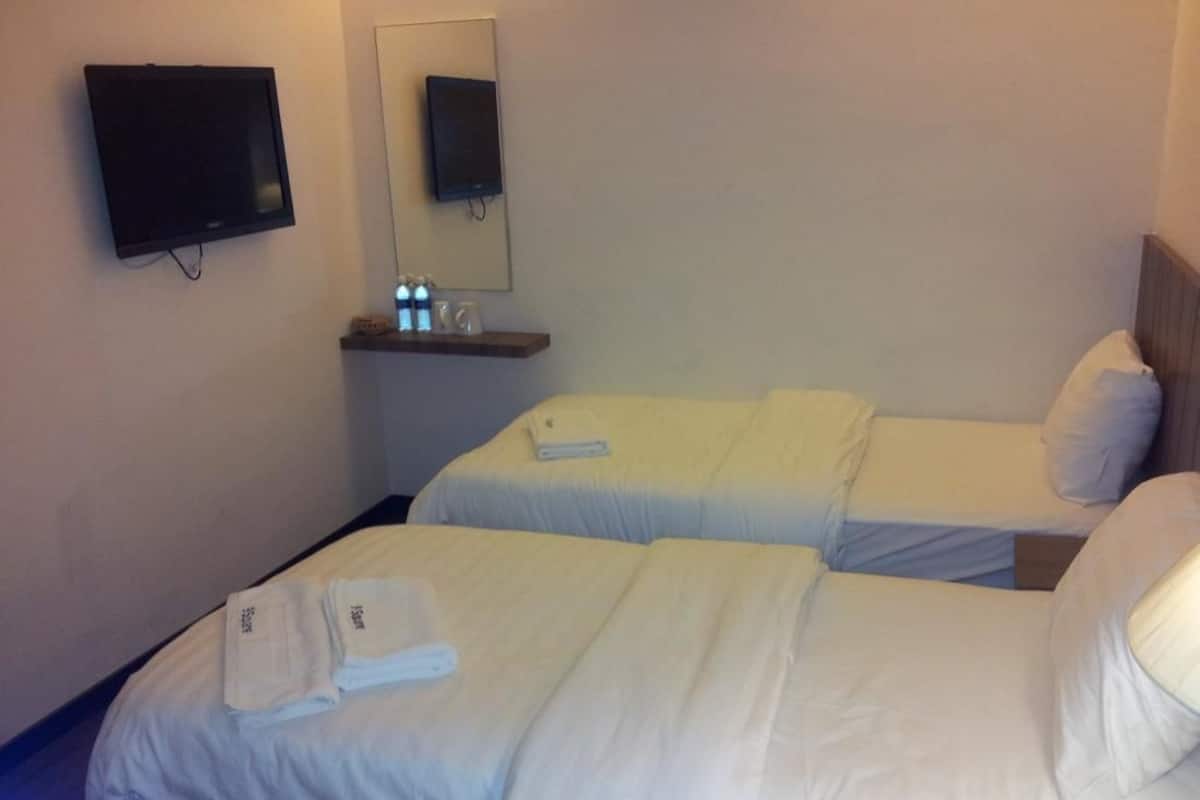 Habitación de hotel con dos camas, un televisor de pantalla plana montado en la pared, una pequeña estantería con artículos de aseo y un espejo sobre la estantería.