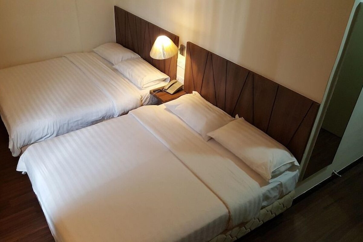 Een hotelkamer met twee enkele bedden, een houten hoofdbord, een bedlampje en een telefoon op het nachtkastje.
