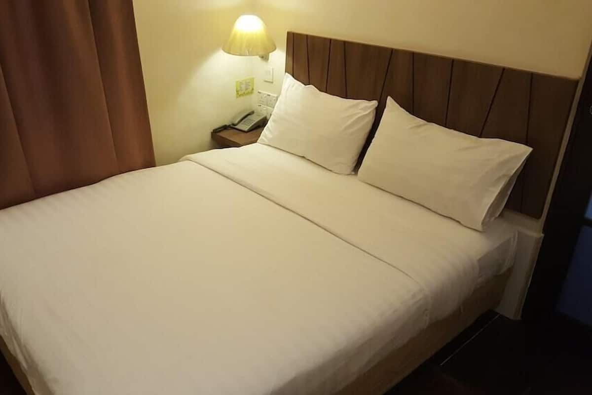Una habitación de hotel con cama, mesita de noche, lámpara y cortina.