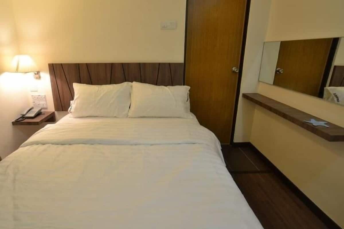 Habitación de hotel con cama, mesita de noche con teléfono, puerta de madera y espejo sobre la cama.