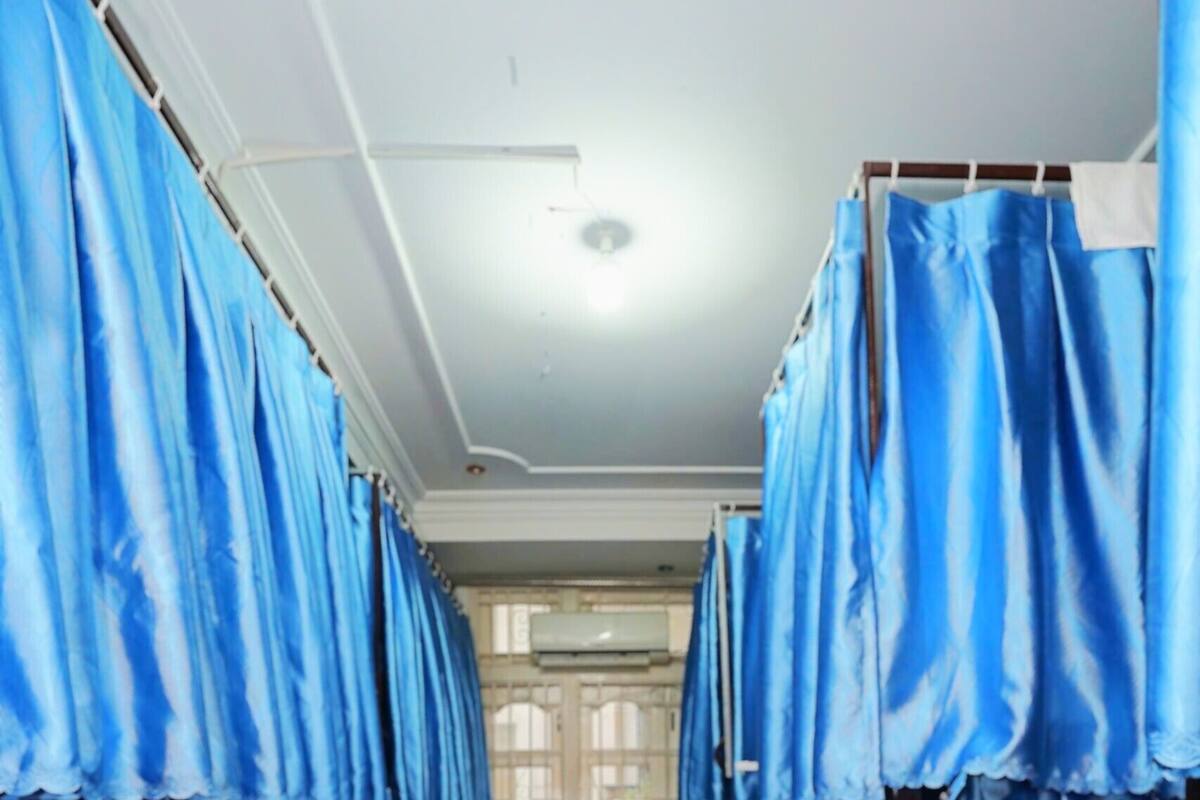 A corridor with rows of blue-covered beds, a tiled floor, and a window with blinds.