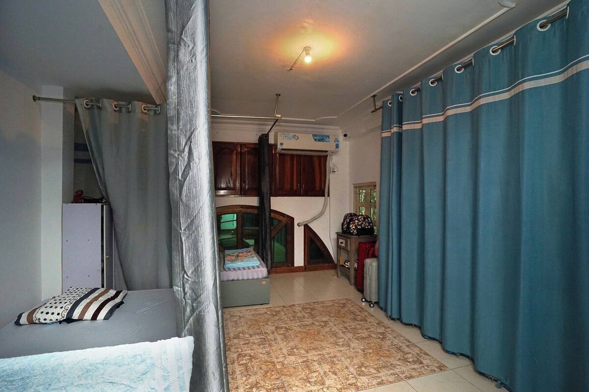 A bedroom with a bed, a desk, a chair, a wardrobe, and a window with curtains.