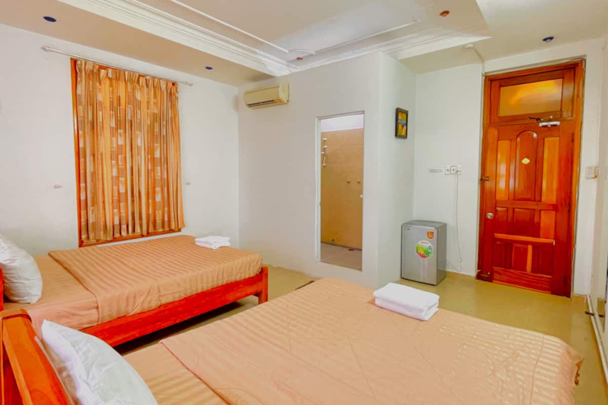 A hotel room with two single beds, a small refrigerator, a wooden door, and a mirror.