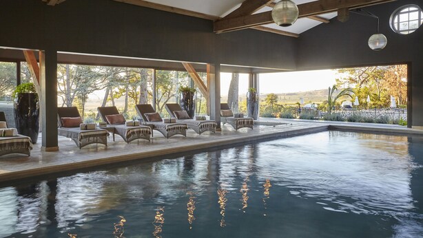 Piscina interior con sillones de descanso y plantas en macetas.
