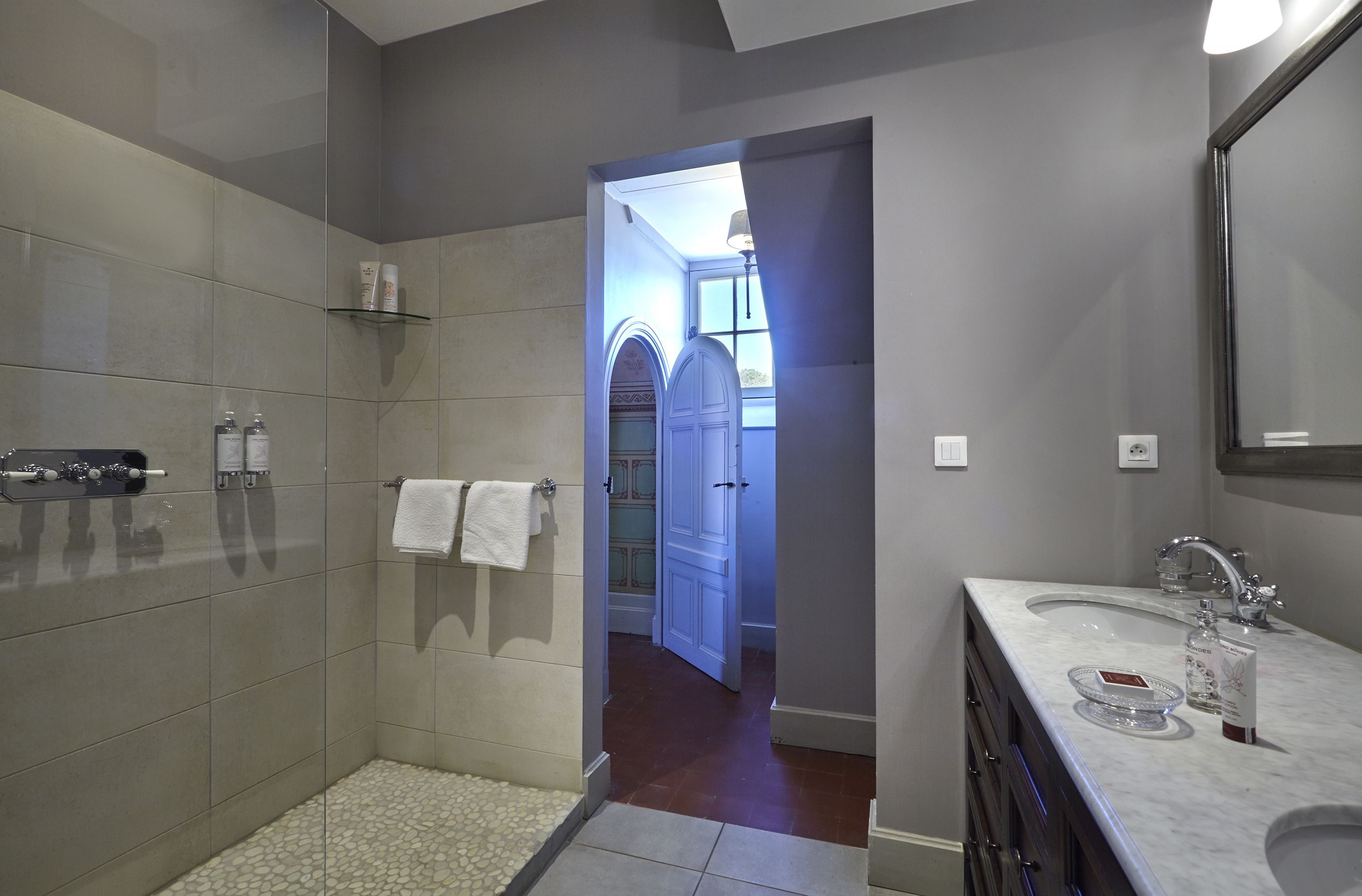 A modern bathroom with a shower, vanity, and a view into a hallway.