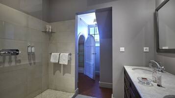 A modern bathroom with a shower, vanity, and a view into a hallway.