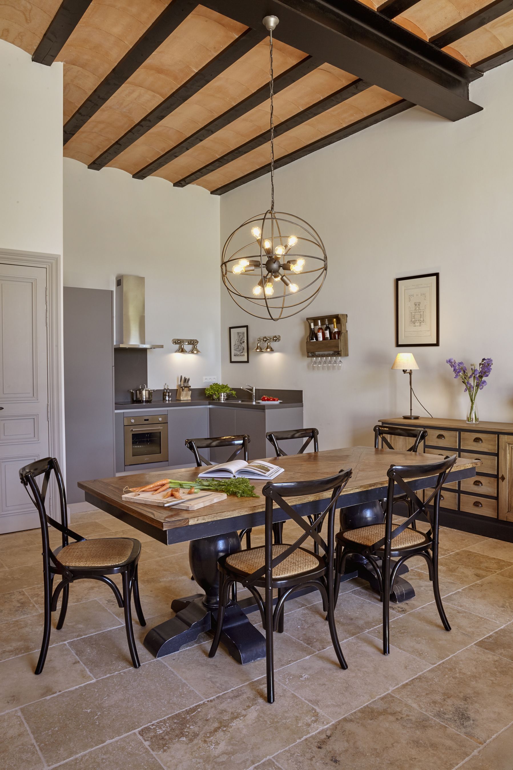 Une cuisine moderne avec un plafond en bois, un îlot central et un coin repas comprenant une grande table et des chaises.