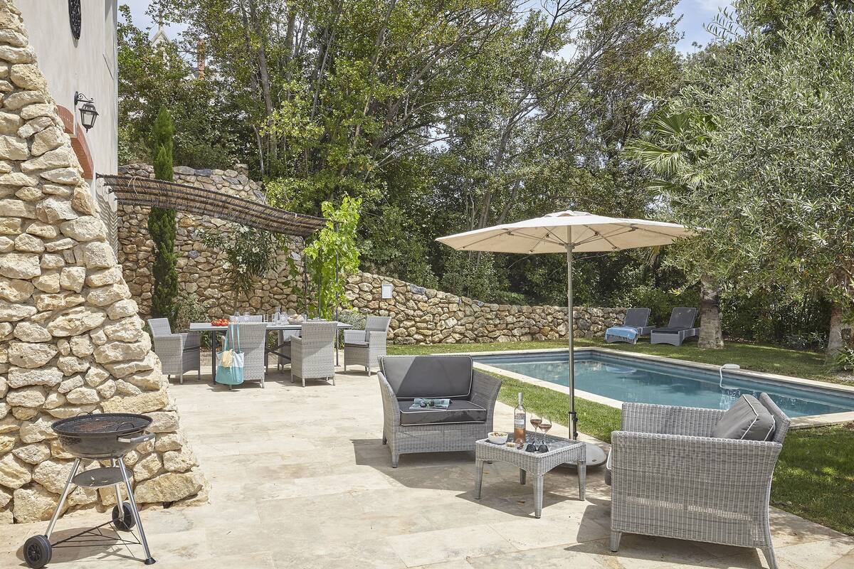 An outdoor patio area with a pool, stone wall, wicker furniture, and a grill.