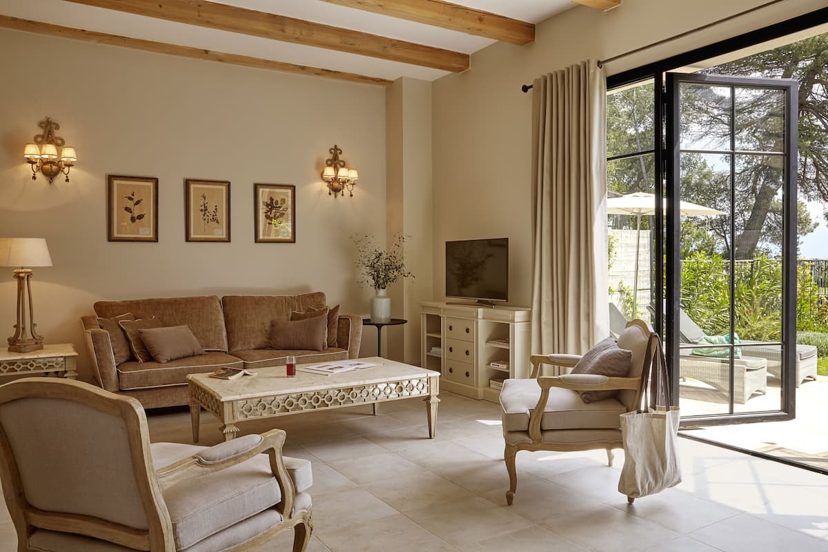 A living room with a sofa, coffee table, and chairs, a television, and a large window with curtains.