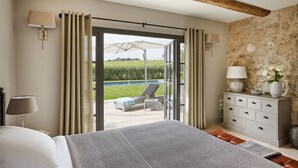 Un dormitorio con cama, cómoda, mesita de noche, ventana con cortinas y vista a una piscina y jardín.