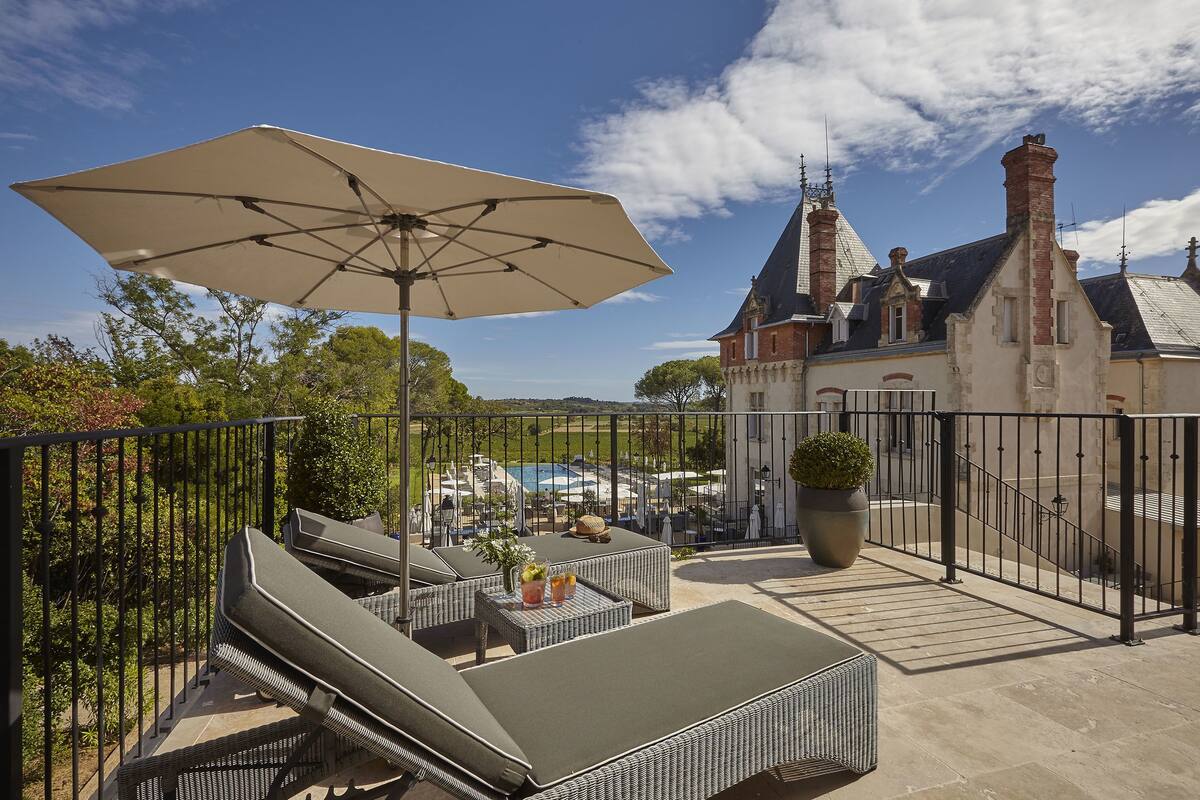 A balcony with outdoor furniture, a large umbrella, and a view of a building with multiple chimneys.
