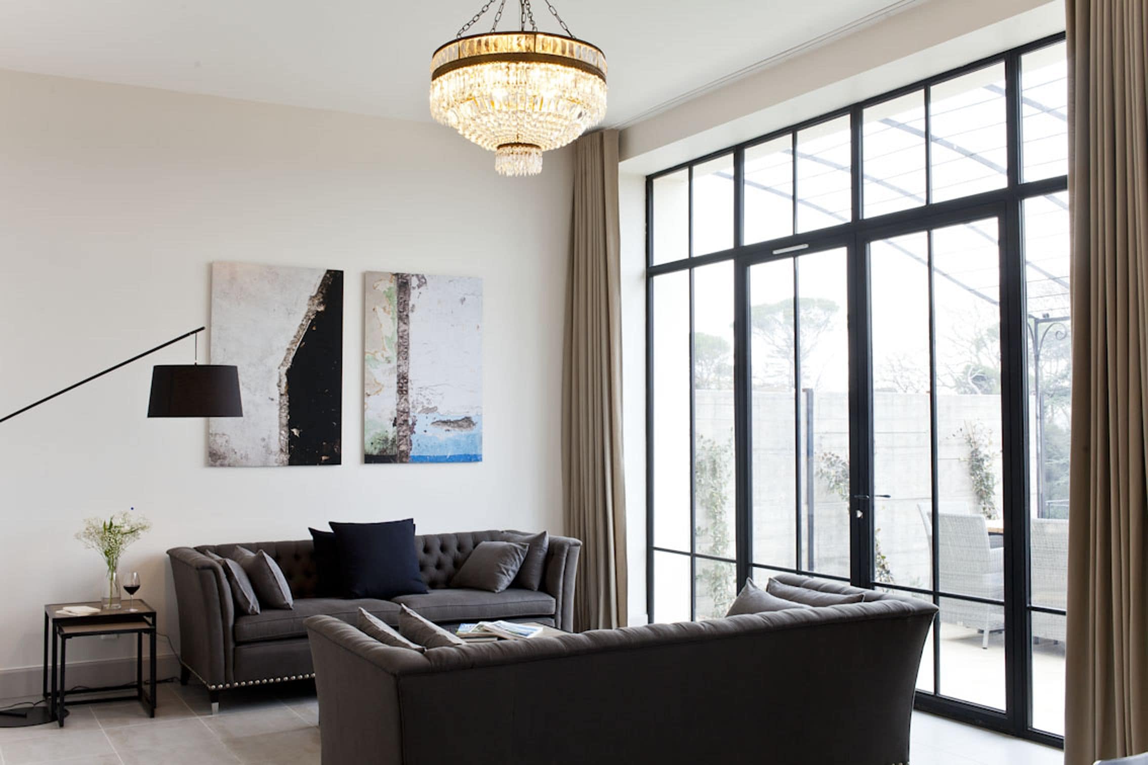 A modern living room with a large window, a chandelier, and two pieces of abstract art on the wall.