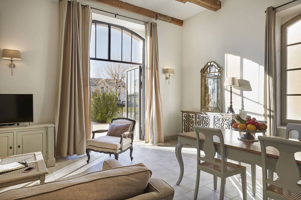 A spacious living room with a large window, a television, a dining table with chairs, and a sofa.