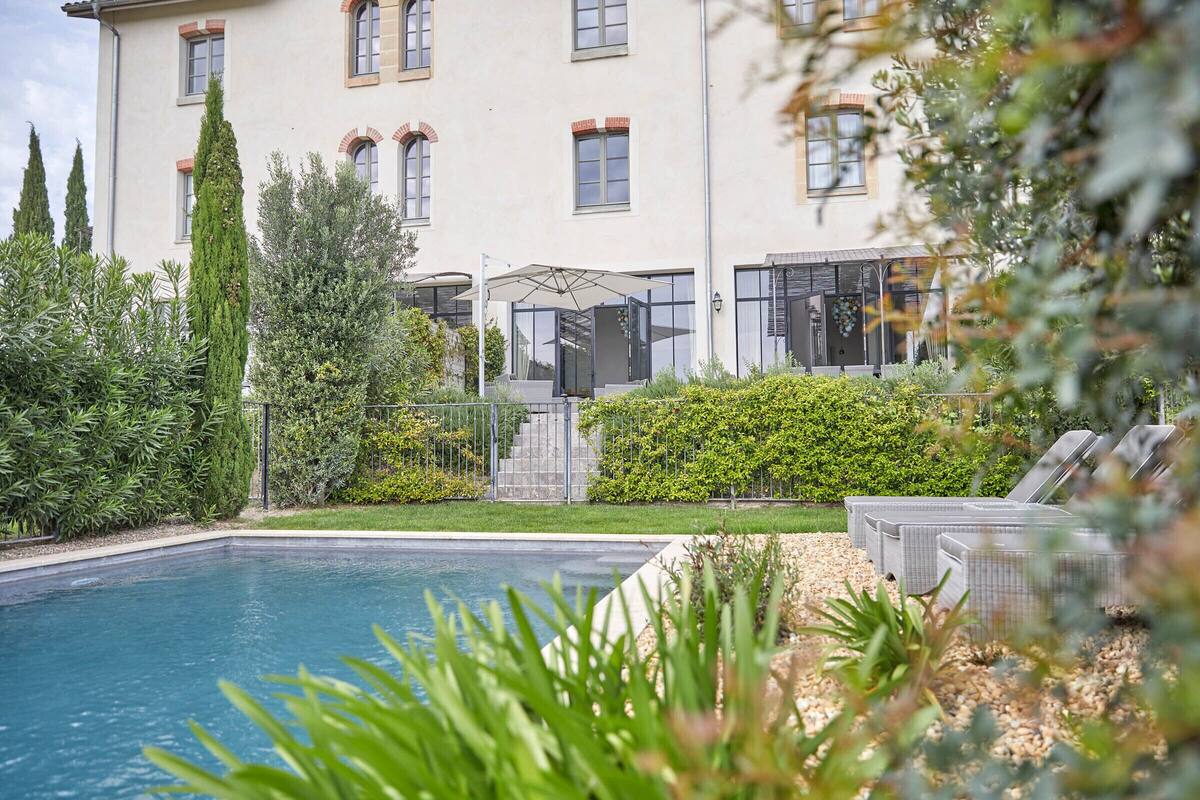A pool area with a clear view of the pool, lounge chairs, and a building with multiple windows and a covered patio.