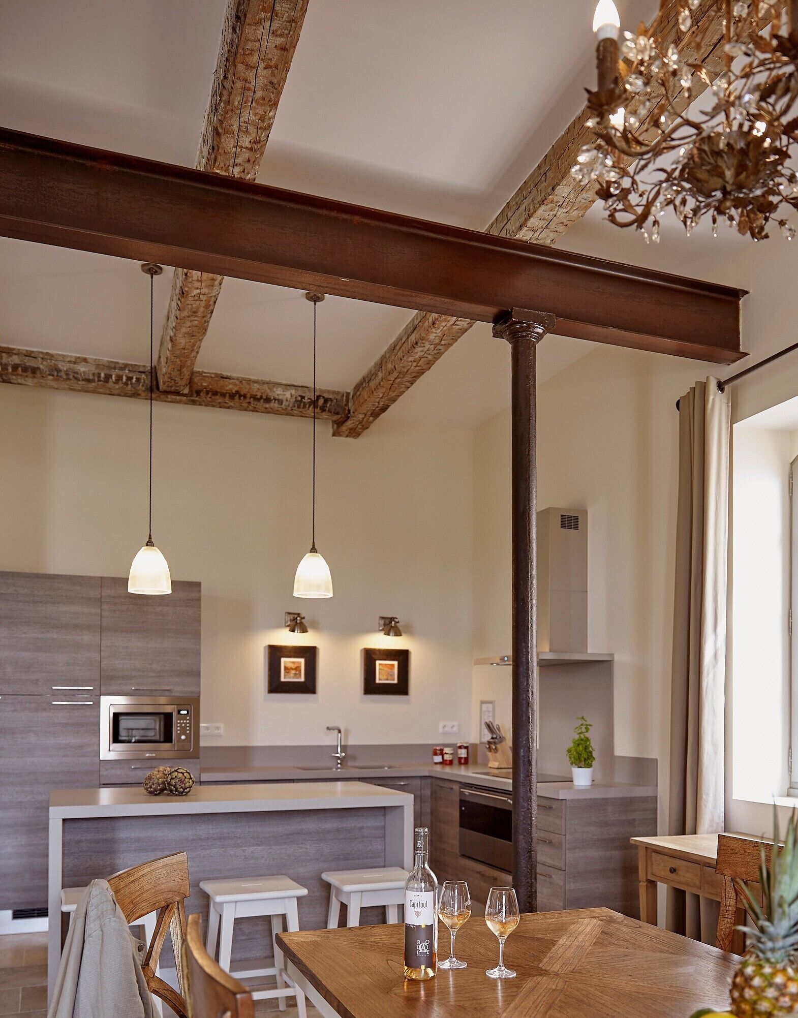 Une cuisine moderne dotée d’un îlot central, de luminaires suspendus et de poutres apparentes en bois.