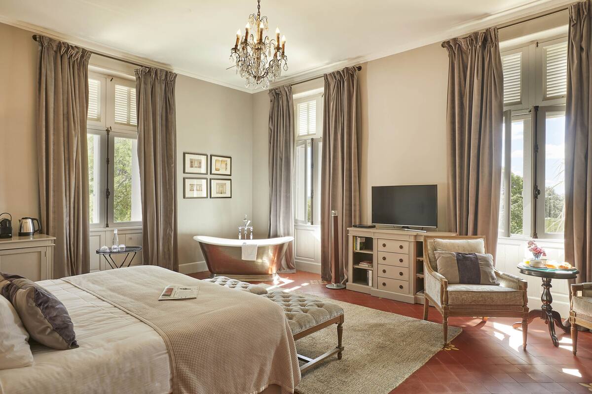 A bedroom with a large bed, a vanity, a bathtub, a desk, and a television.