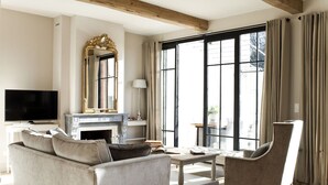 Una sala de estar con sofá, sillón, mesa de centro, chimenea, televisor y ventanas grandes con cortinas.