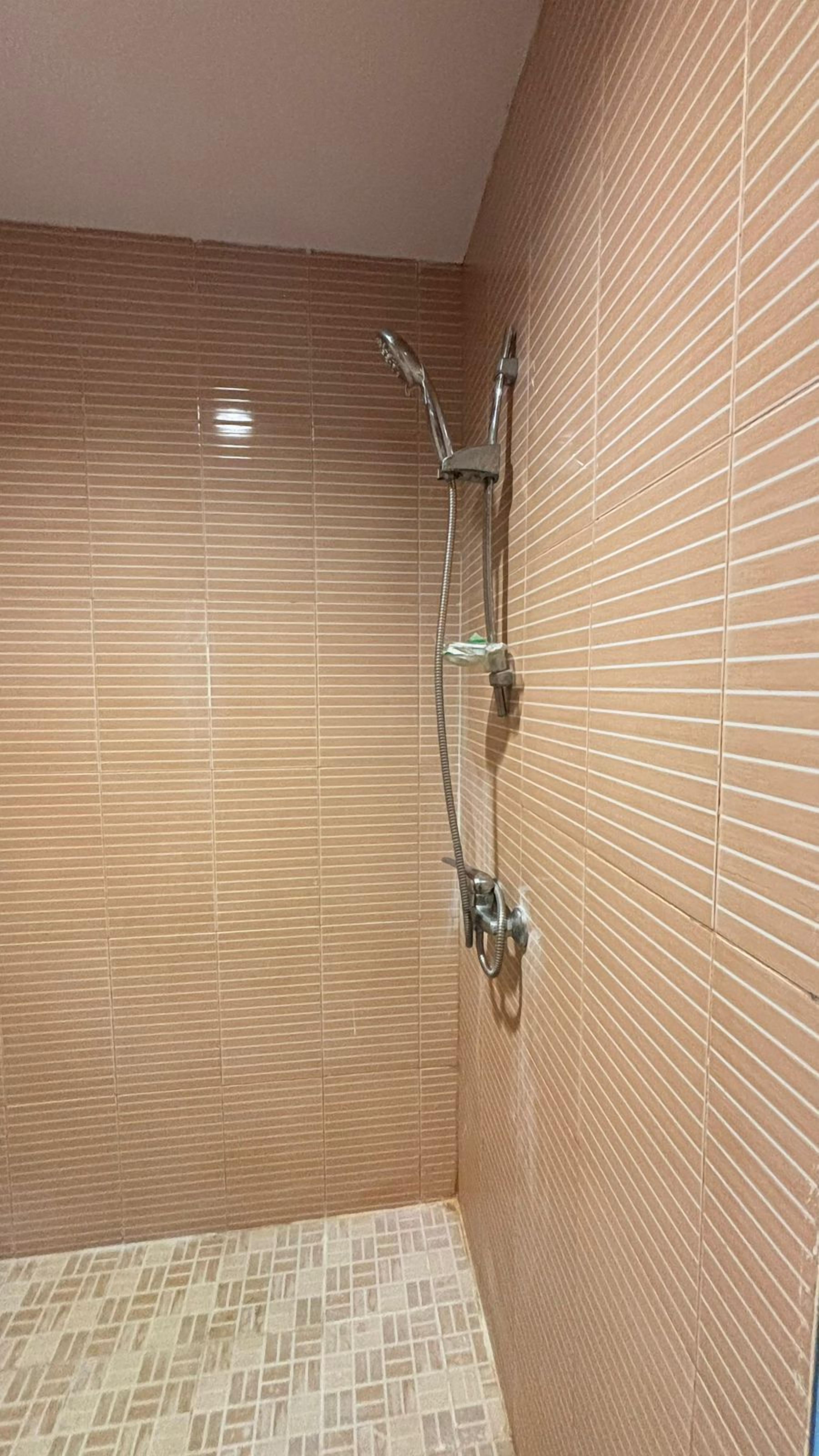 A shower area with a tiled wall and floor, a handheld showerhead, and a wall-mounted faucet.
