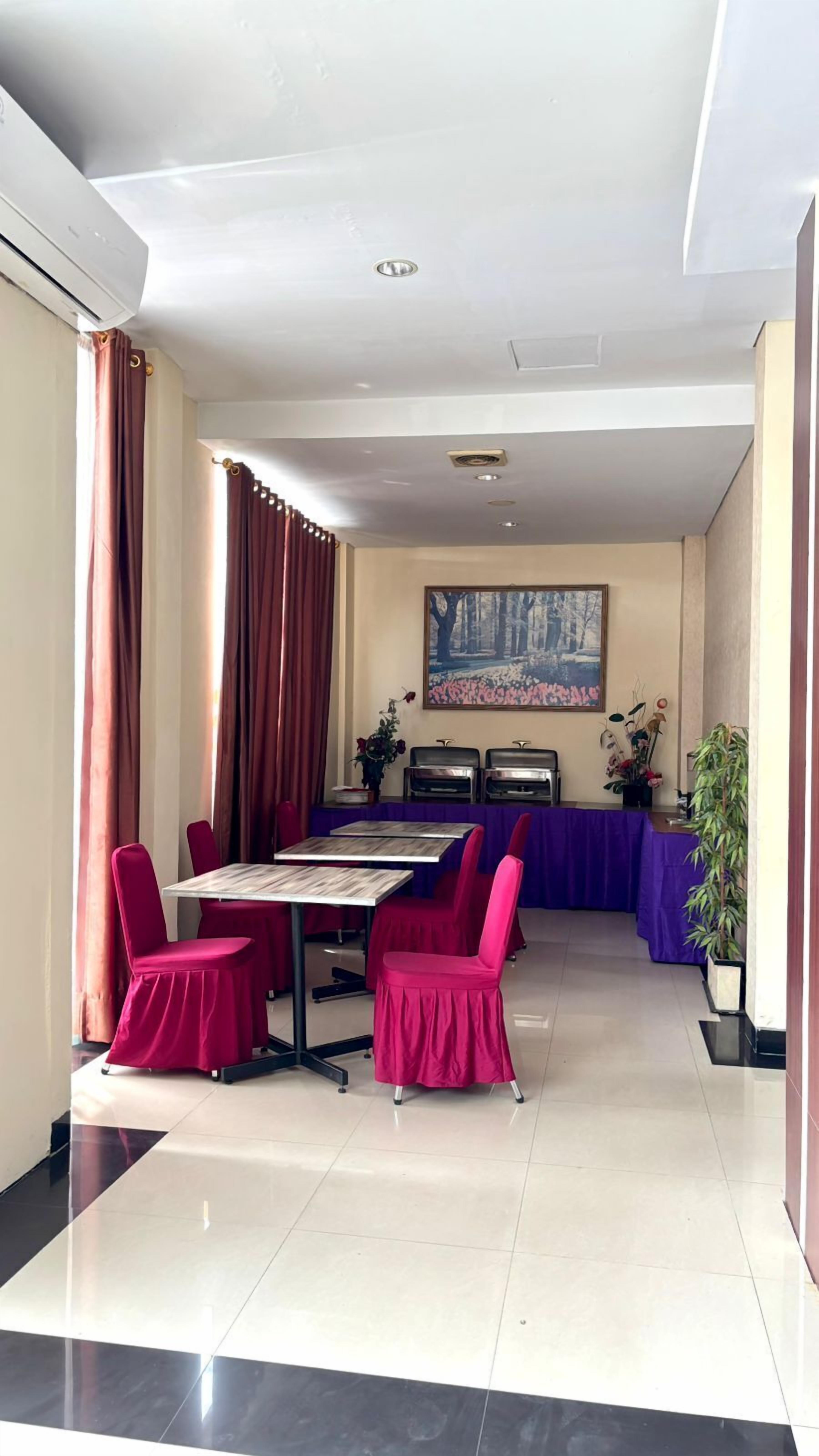 A dining area with a long table, red chairs, a painting on the wall, and a buffet station.