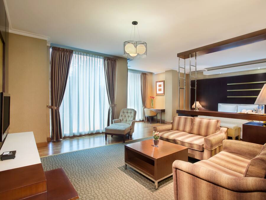A modern hotel room with a sofa set, a coffee table, a TV, and a desk with a lamp.