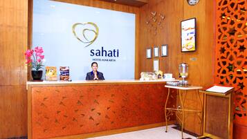 A reception desk at Sahati Hotel Jakarta with a modern design, a heart logo, and framed certificates on the wall.