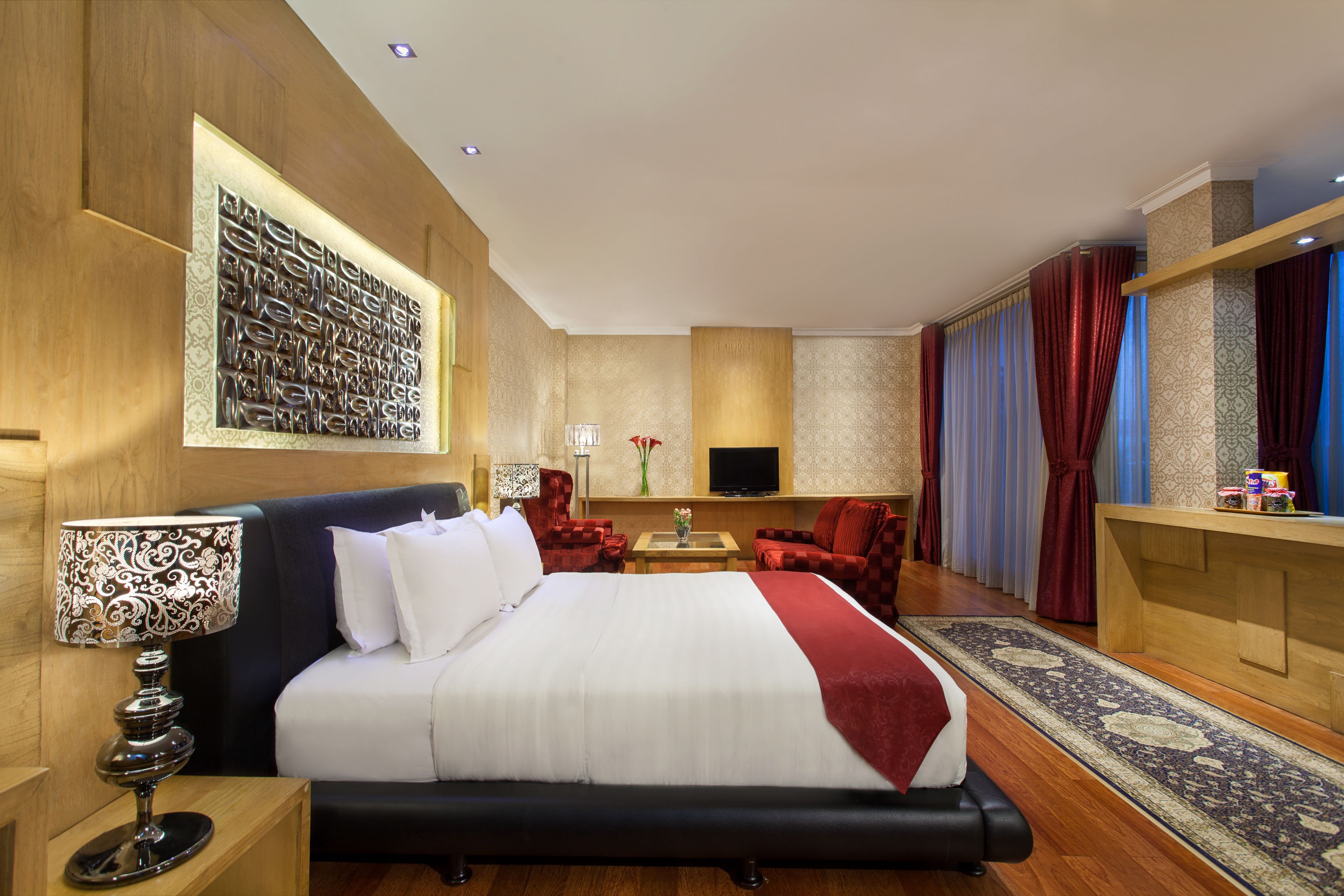 A hotel room with a large bed, a desk, a TV, and a seating area with chairs.