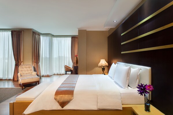 A hotel room with a large bed, a chair, a desk, and a vase with flowers. - Sahati Hotel (Jakarta)