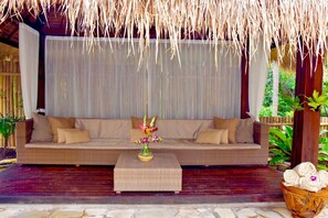 An outdoor seating area with a woven sofa, a small table with a vase of flowers, and a basket of towels.