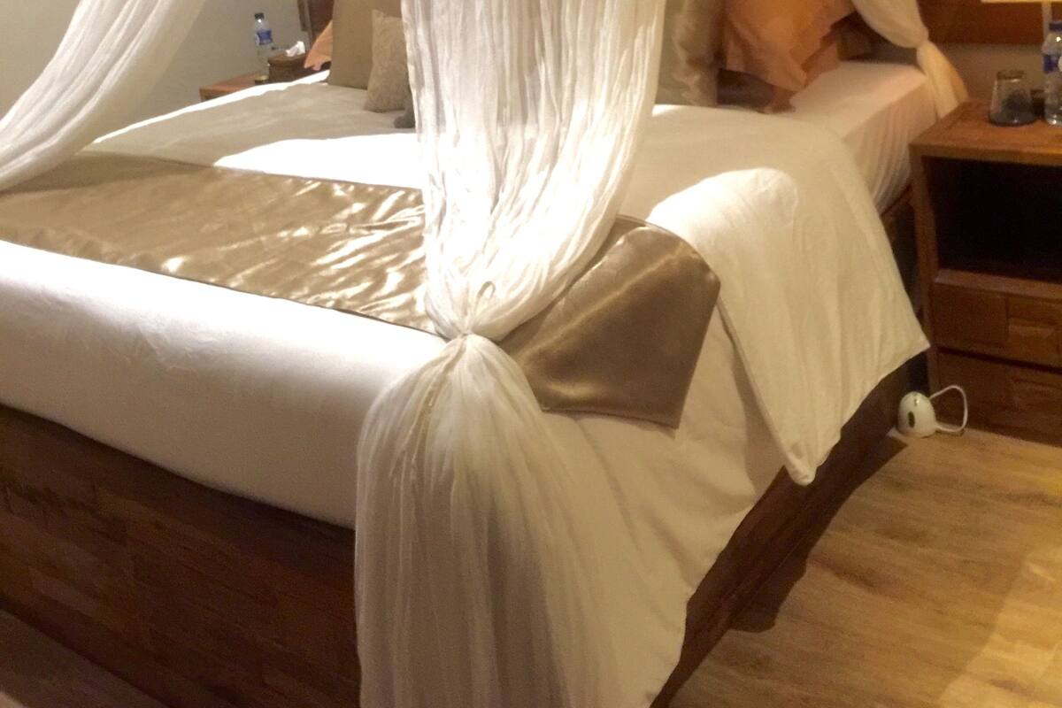 Un lit à baldaquin, une table de chevet avec une lampe et une petite table de nuit avec un chargeur de téléphone.