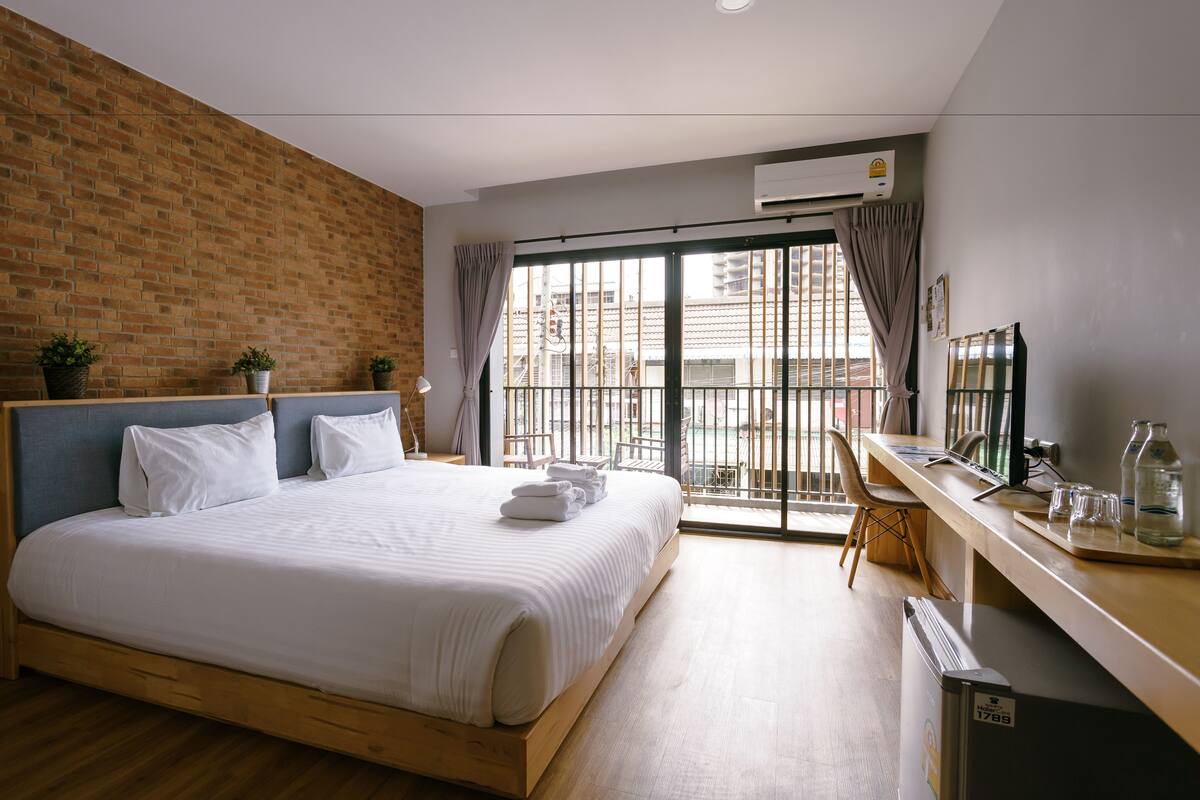 Habitación de hotel moderna con una cama grande, un escritorio con computadora y vistas a la ciudad a través de una puerta corredera.