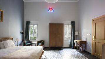 Habitación de hotel con cama, escritorio, silla, armario y dos ventanas con cortinas.