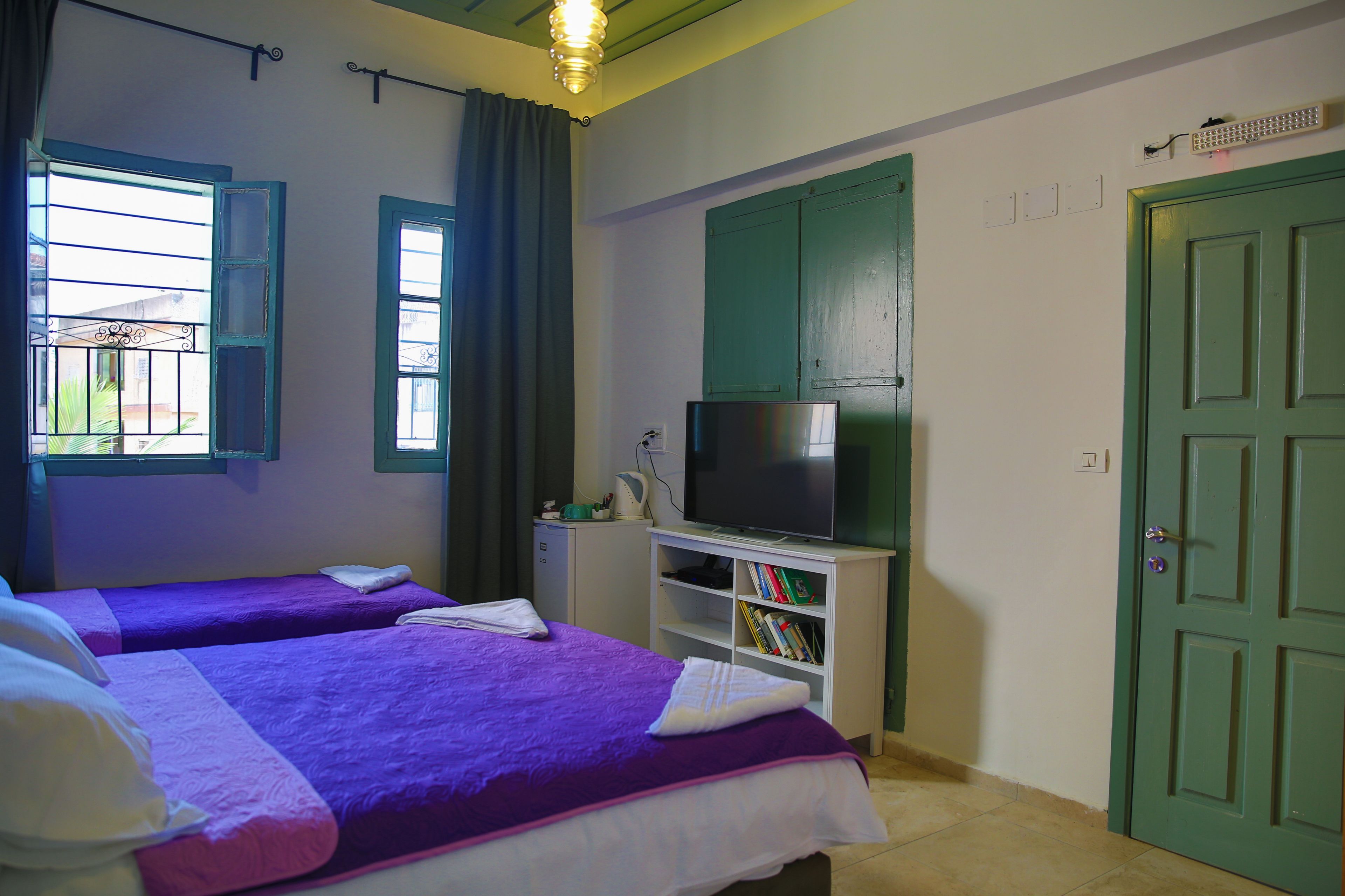A hotel room with two beds, a television, a bookshelf, and a green door.