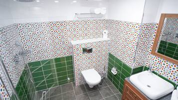 Un baño con ducha, inodoro y lavamanos, con azulejos blancos y verdes con estampado.