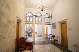 A spacious hallway with a high ceiling, stone walls, and a chandelier. There are multiple doors, a staircase, and a dining area with chairs and a table.