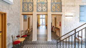 A hotel lobby with a geometric patterned floor, a staircase, and a view into the dining area. - Michel House (Nazareth)