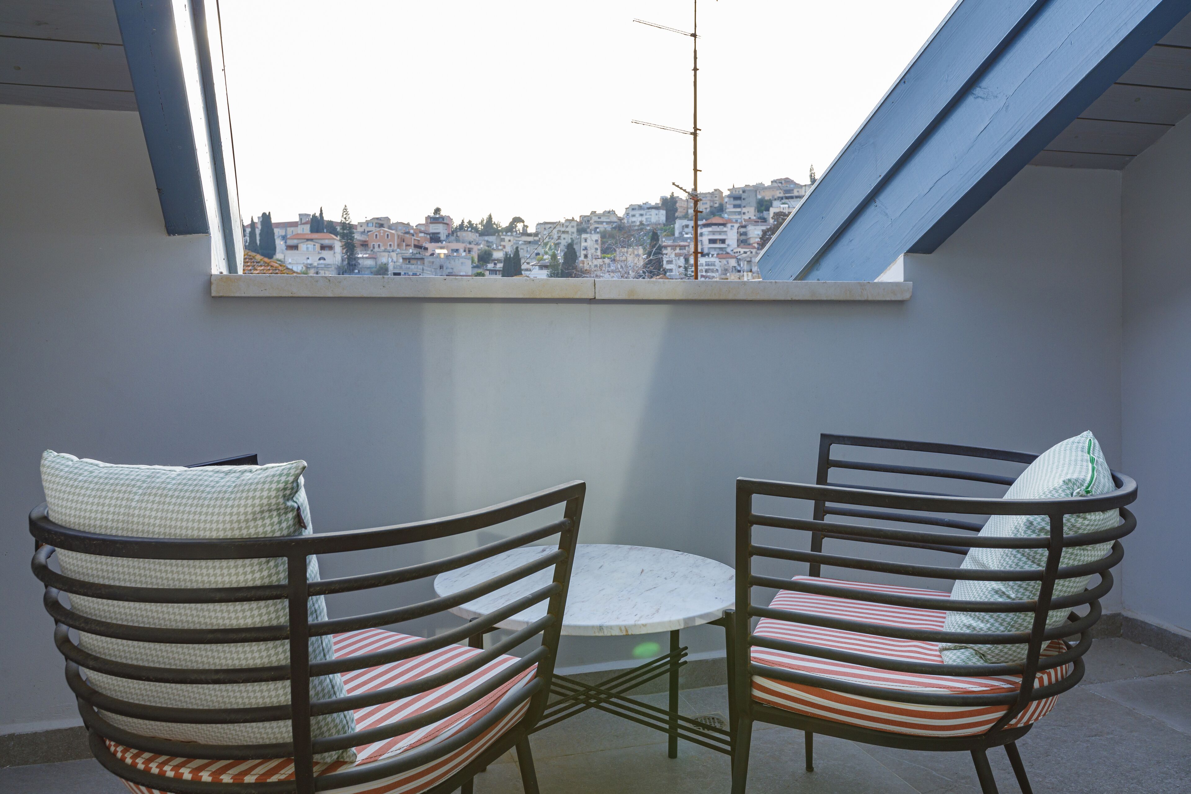Un balcon avec deux chaises et une petite table, donnant sur un paysage urbain.